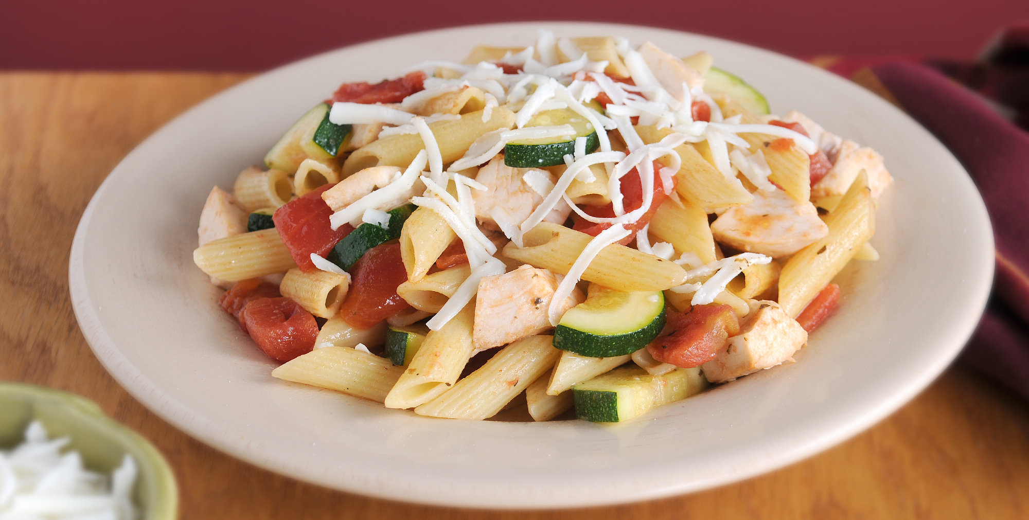 Penne pasta with zucchini, tomatoes, and chicken, topped with shredded cheese